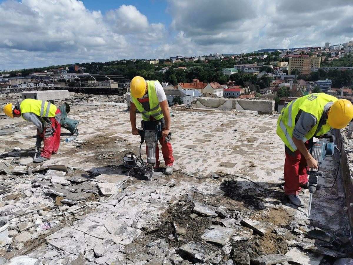 Három munkás elektromos bontókalapáccsal bontja egy többszintes épület lapostetőjének burkolatát és aljzatát